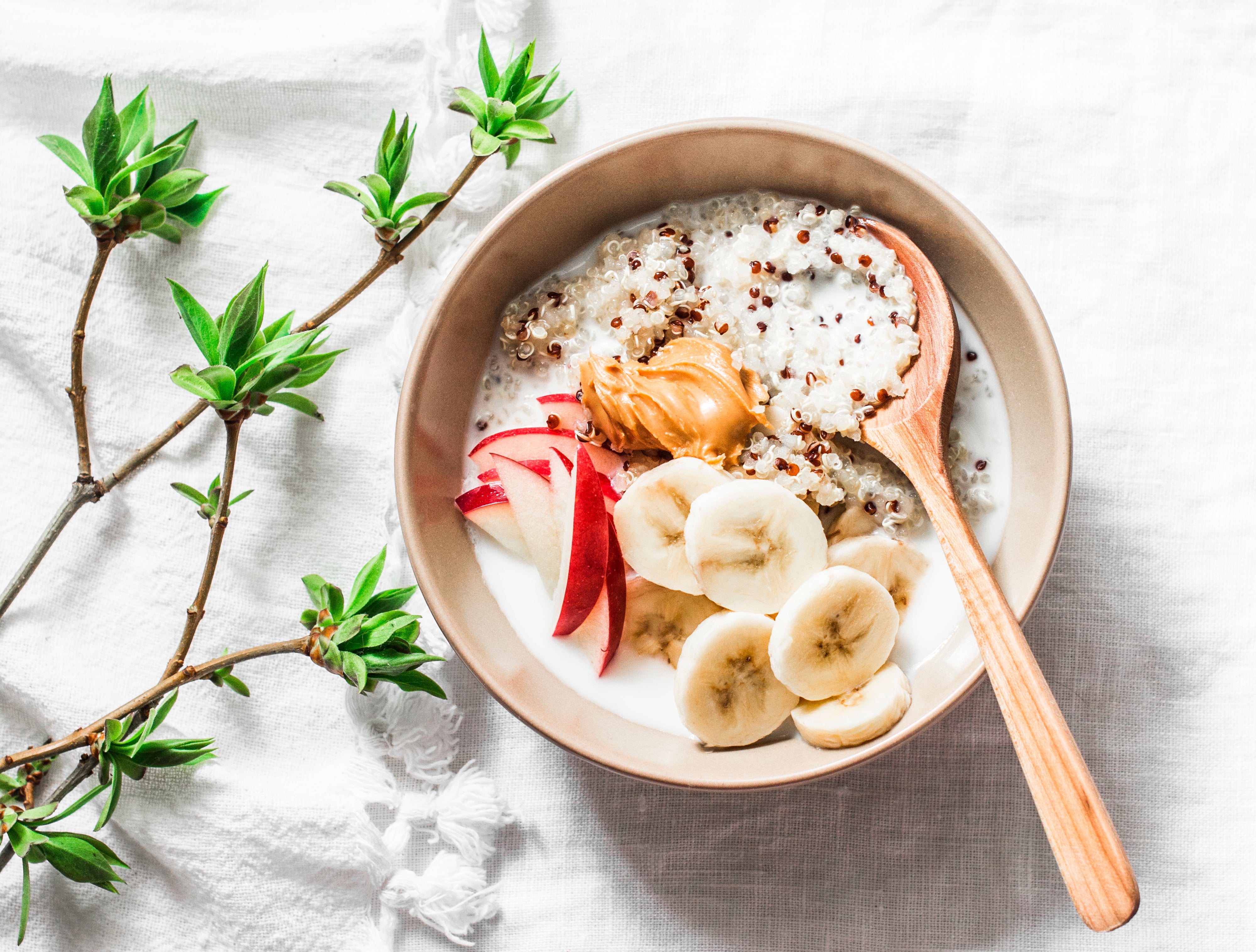 Quinoa, coconut milk, banana, apple, peanut butter porridge on light background, top view. Delicious diet, vegetarian breakfast or snack