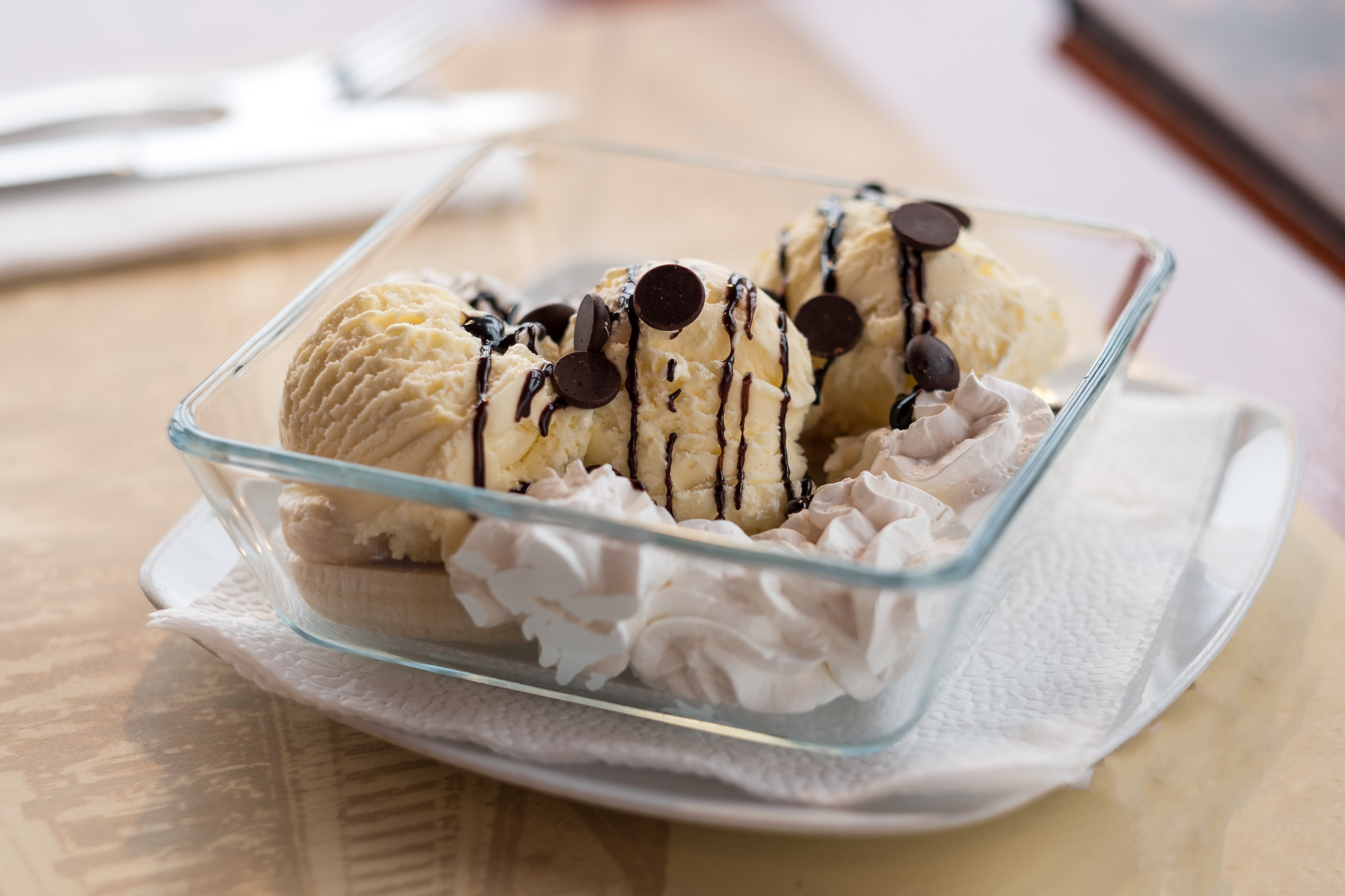 Banana split ice cream sundae on plate with almonds, whipped cream and chocolate topping