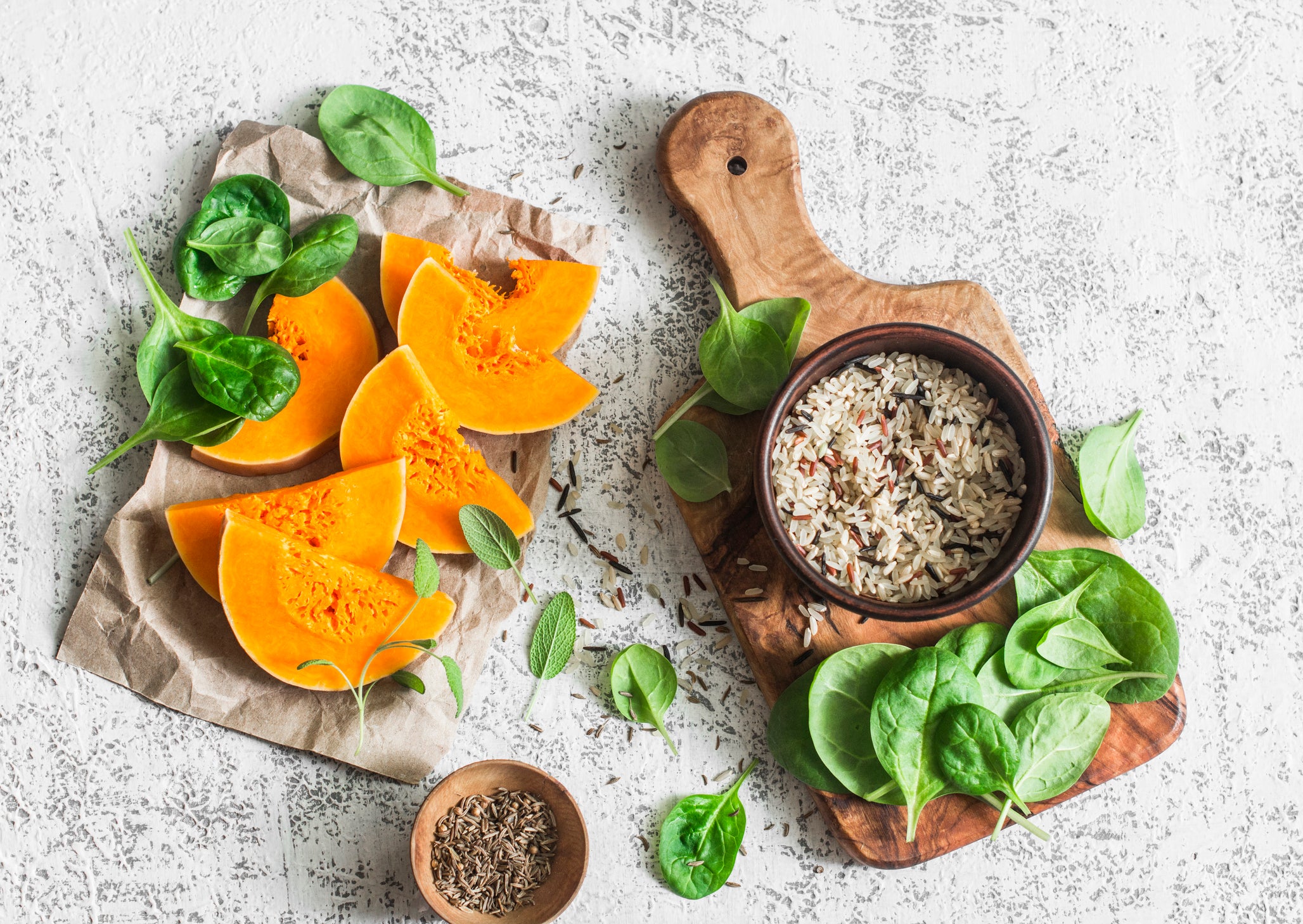 Raw ingredients for cooking vegetarian lunch - pumpkin, wild rice, spinach, spices on a light table, top view. Flat lay