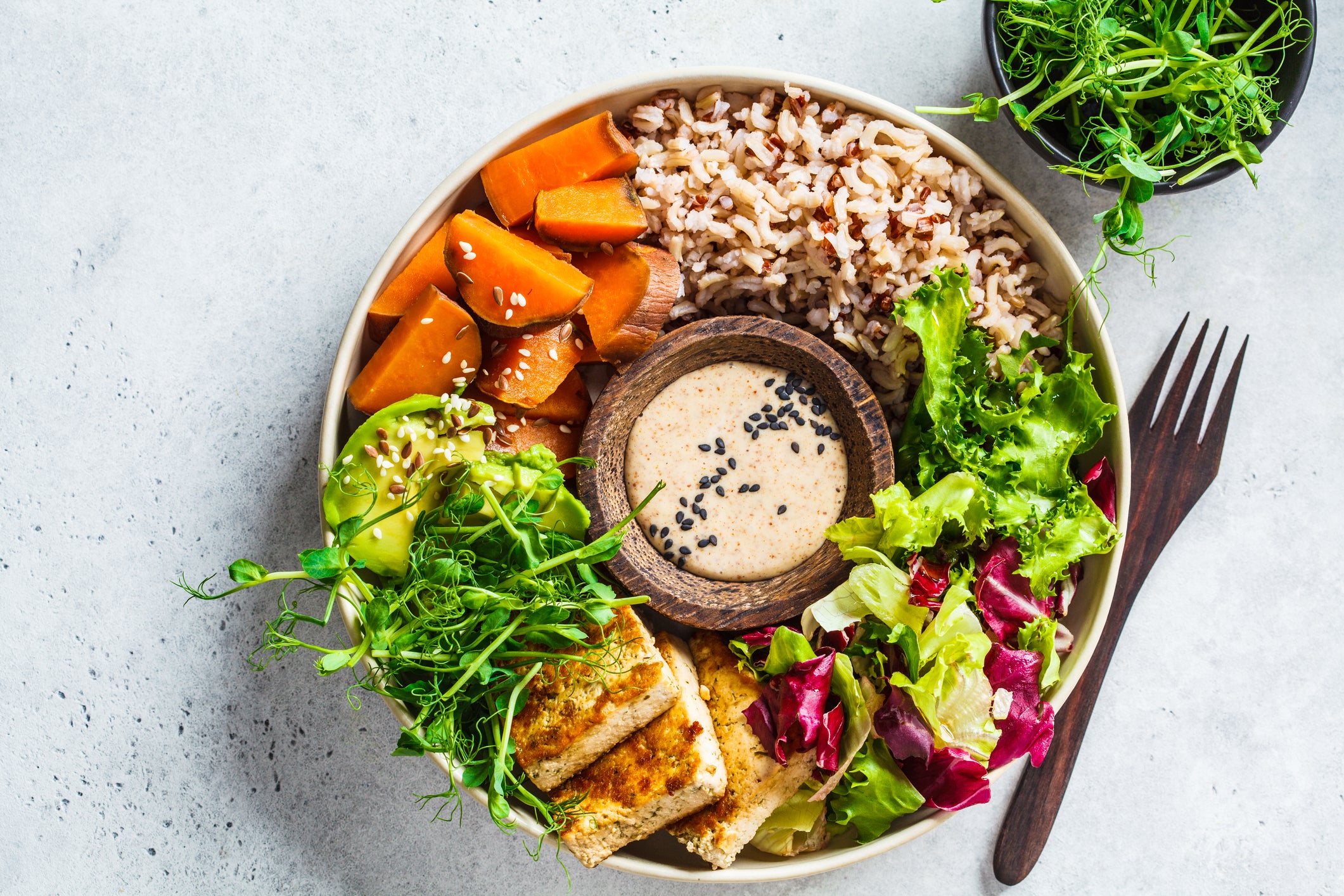 Buddha bowl with tofu, avocado, rice, seedlings, sweet potato and tahini dressing.