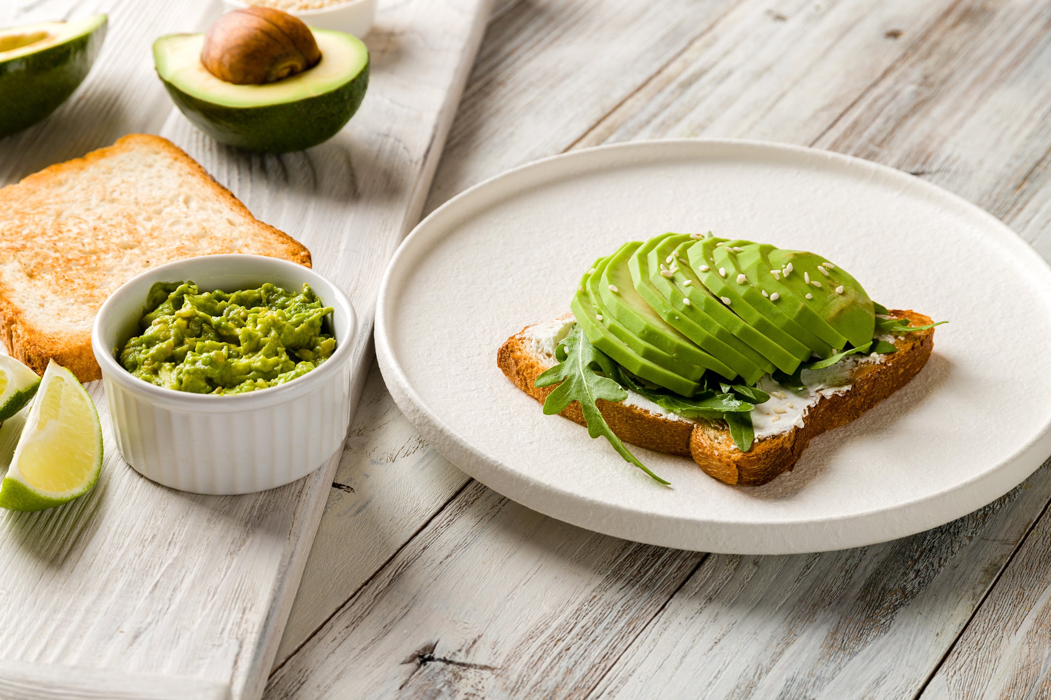 Toast with avocado, cream cheese,guacamole and arugula on white wooden table