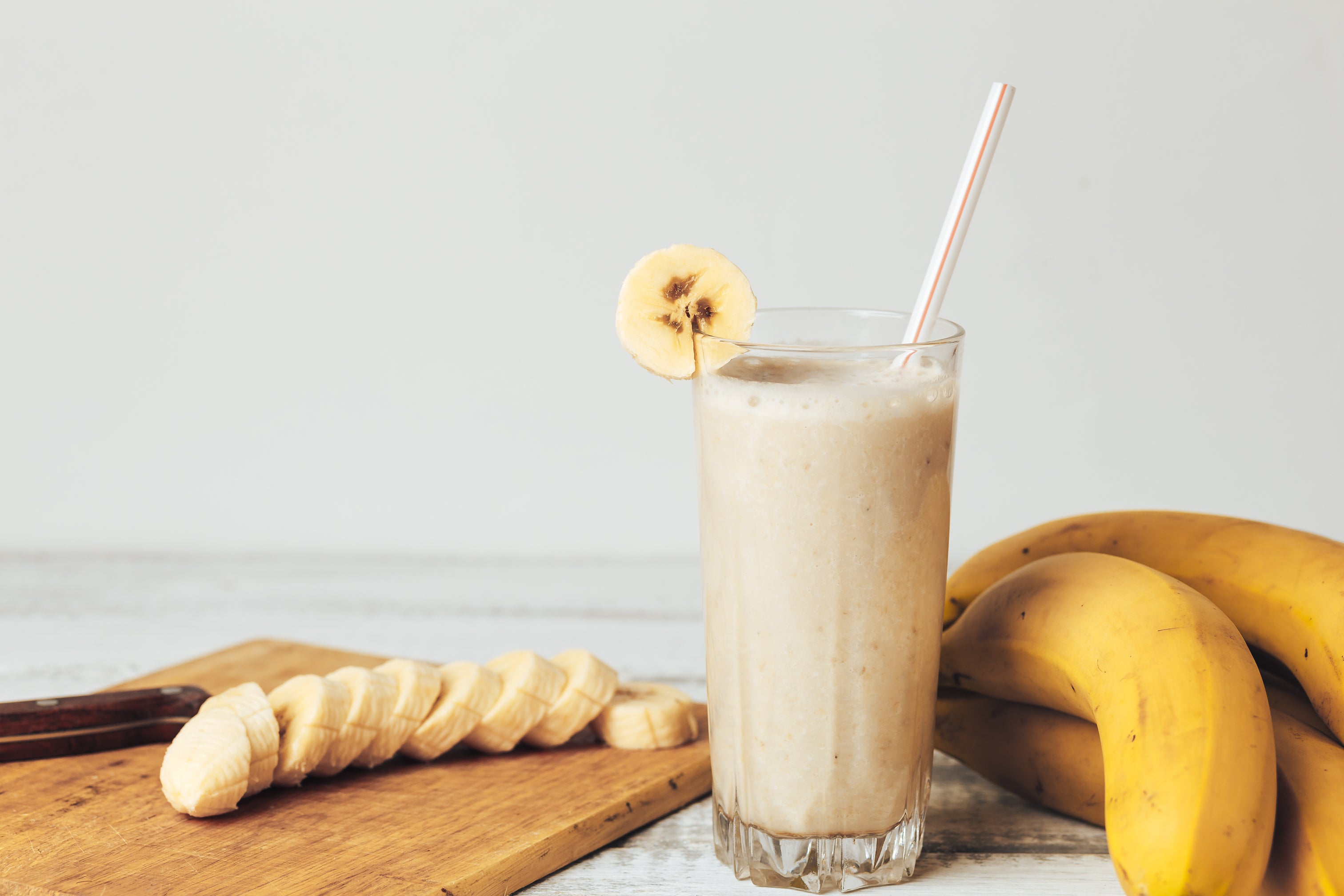 Fresh homemade banana smoothie, cutting board and bananas on white rustic wood