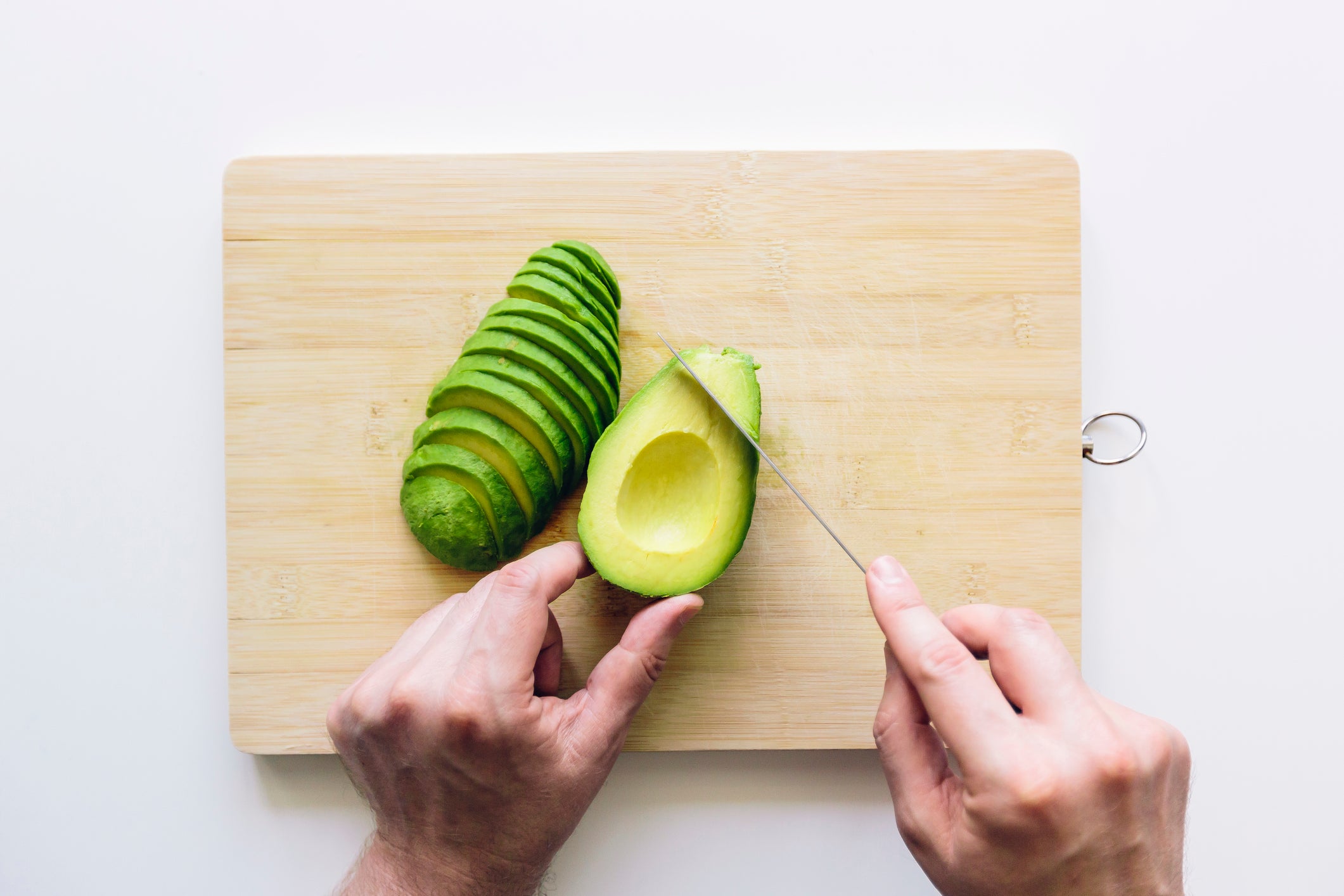 Man cutting avocado on a wooden cutting board, personal perspective directly above view