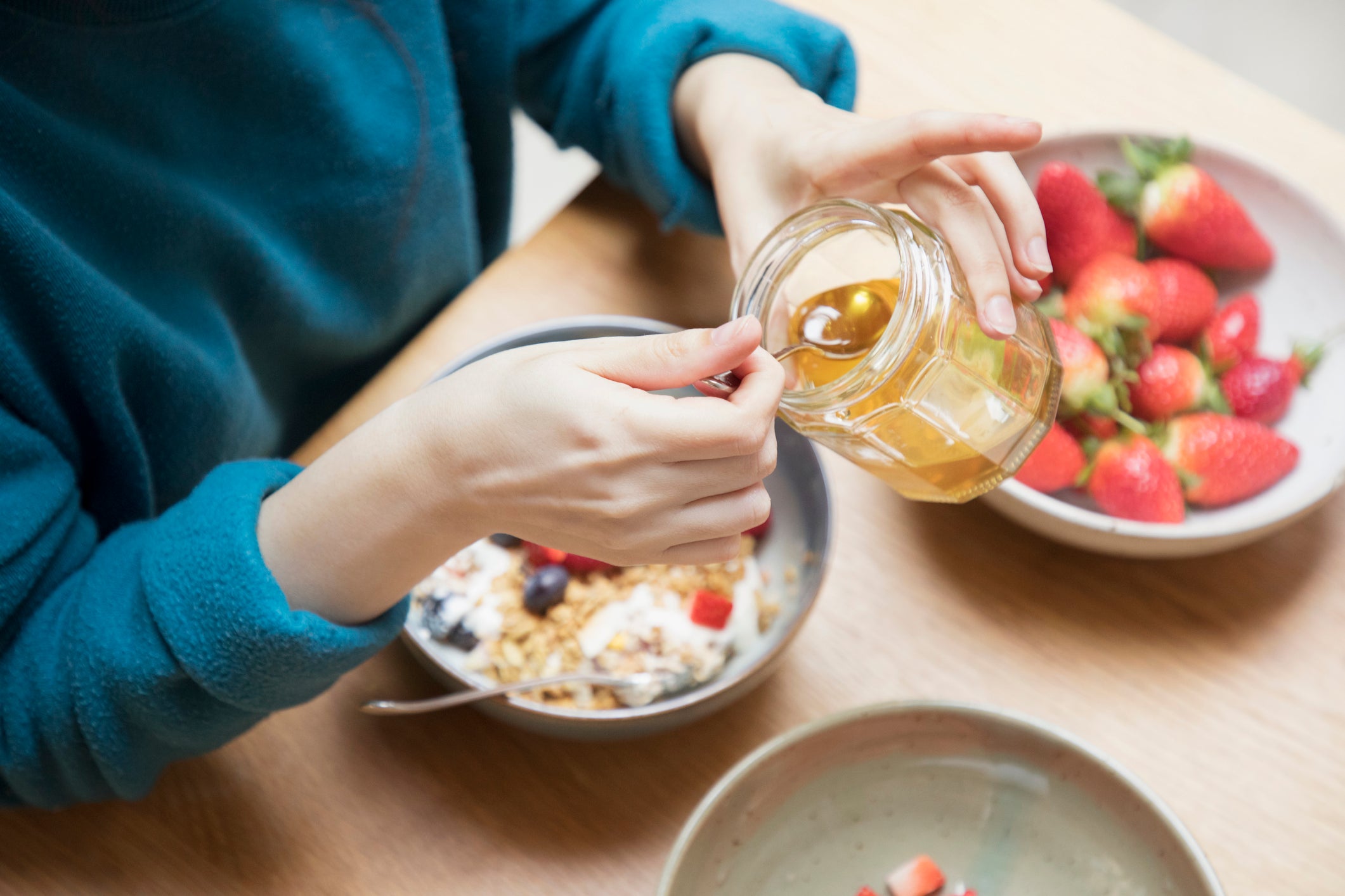 Woman takes honey from jar with spoon for breakfast.