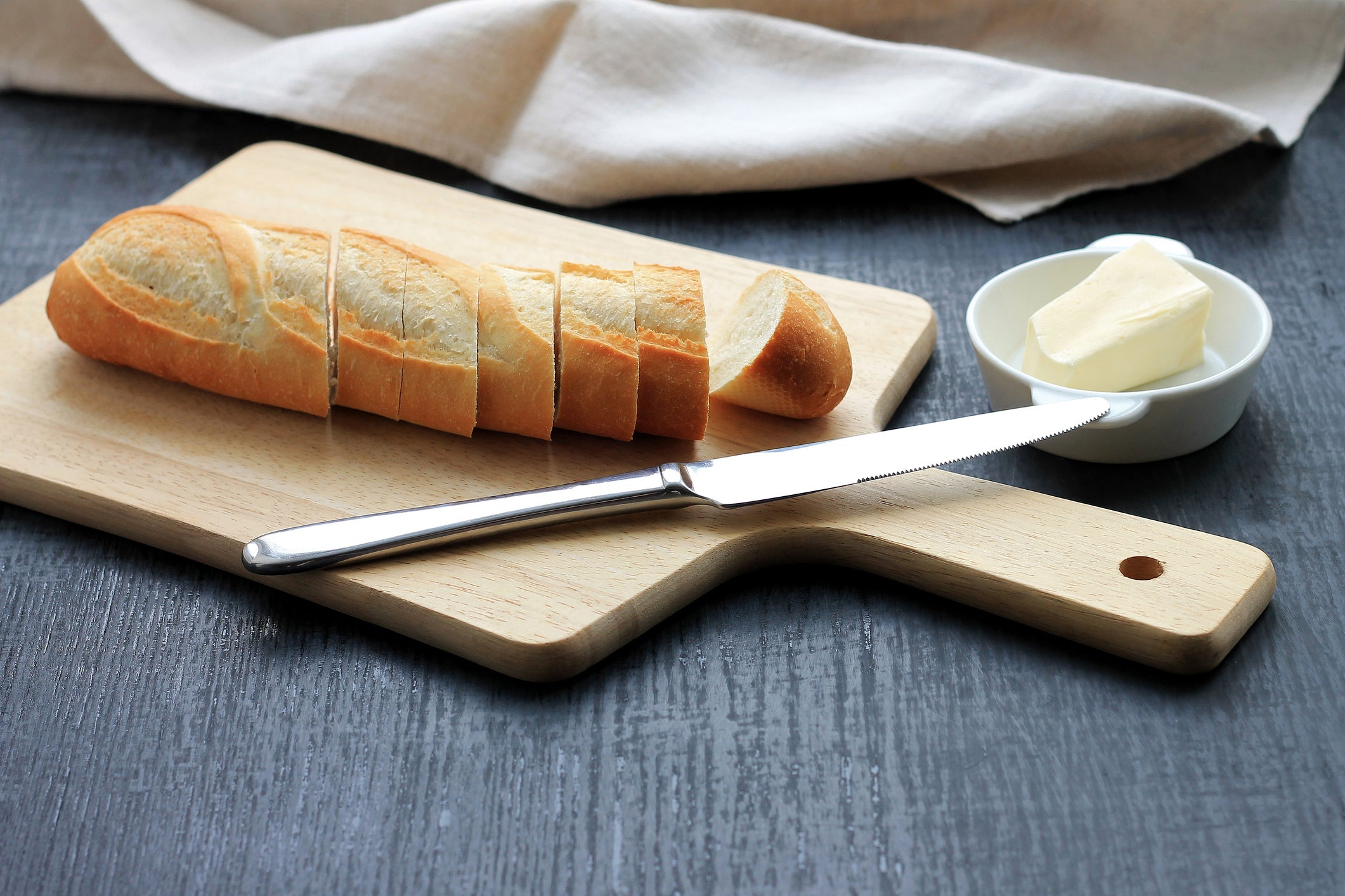 Traditional breakfast. Bread (sliced baguette) on cutting board with butter on plate on dark background.