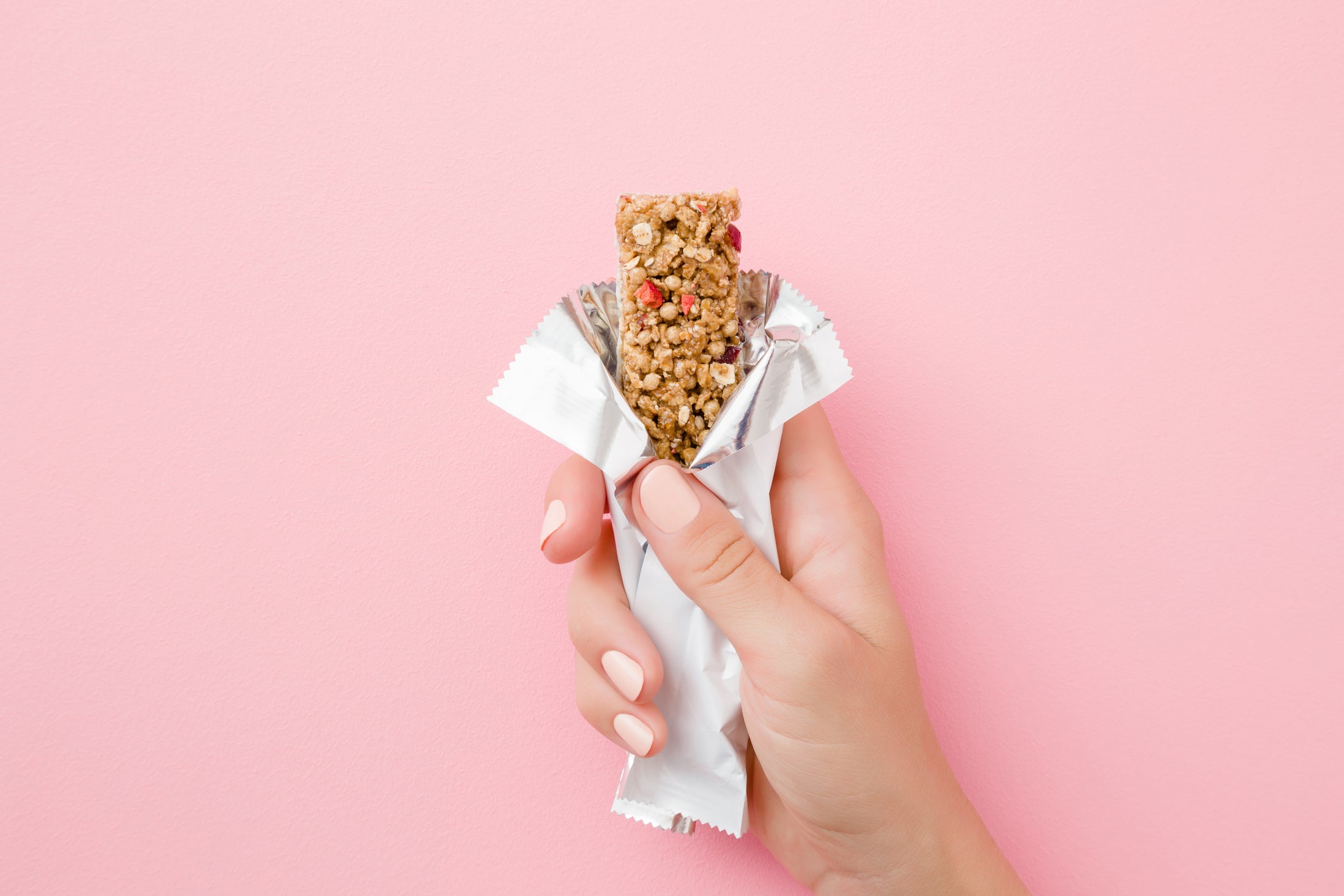 Young woman hand holding cereal bar on pastel pink table. Opened white pack. Closeup. Sweet healthy food. Top view.