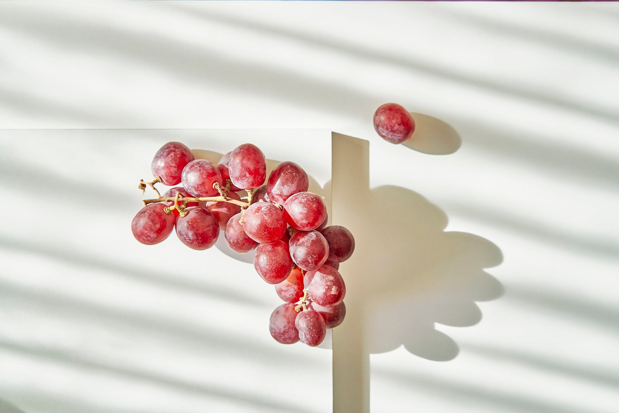 bunch of red grapes on a white table with shadow play