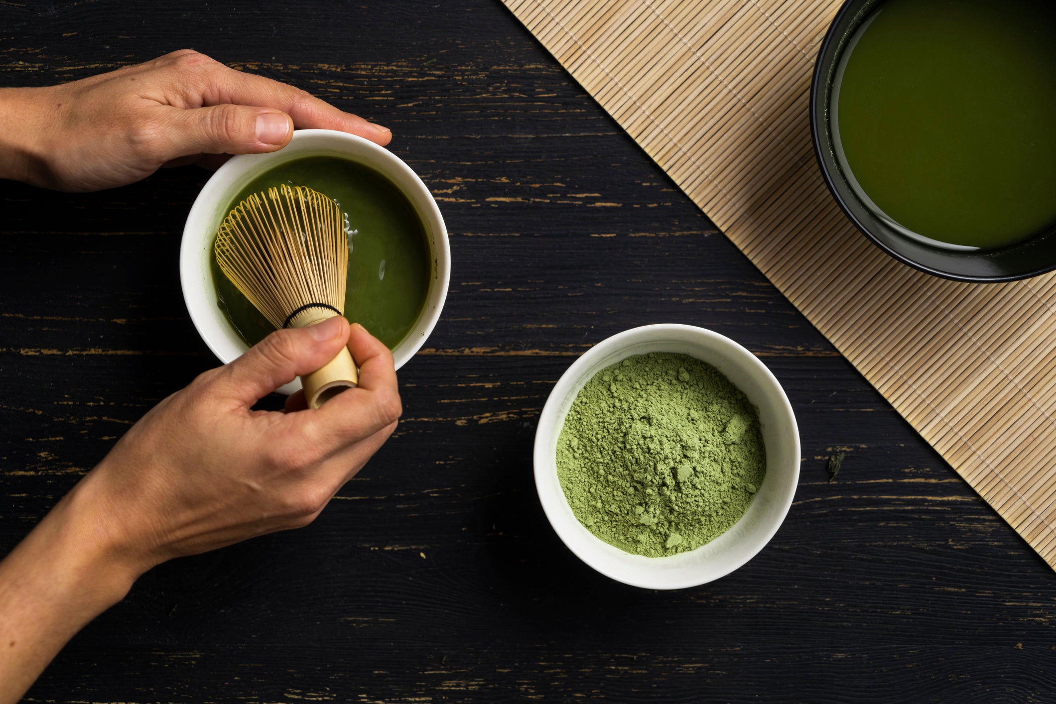 Woman's hands mixing matcha green tea powder in a bowl, overhead view