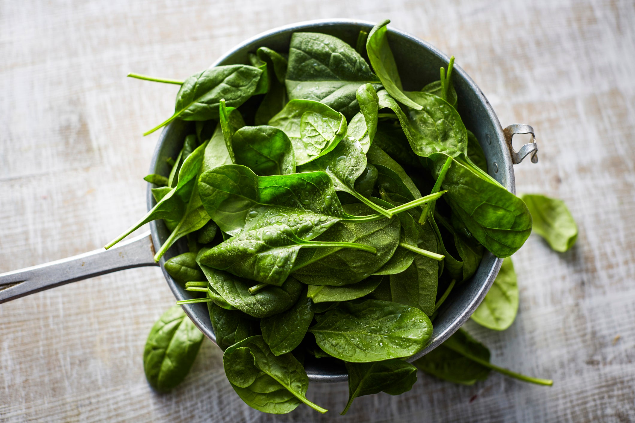 Fresh spinach leaves in colander on wood