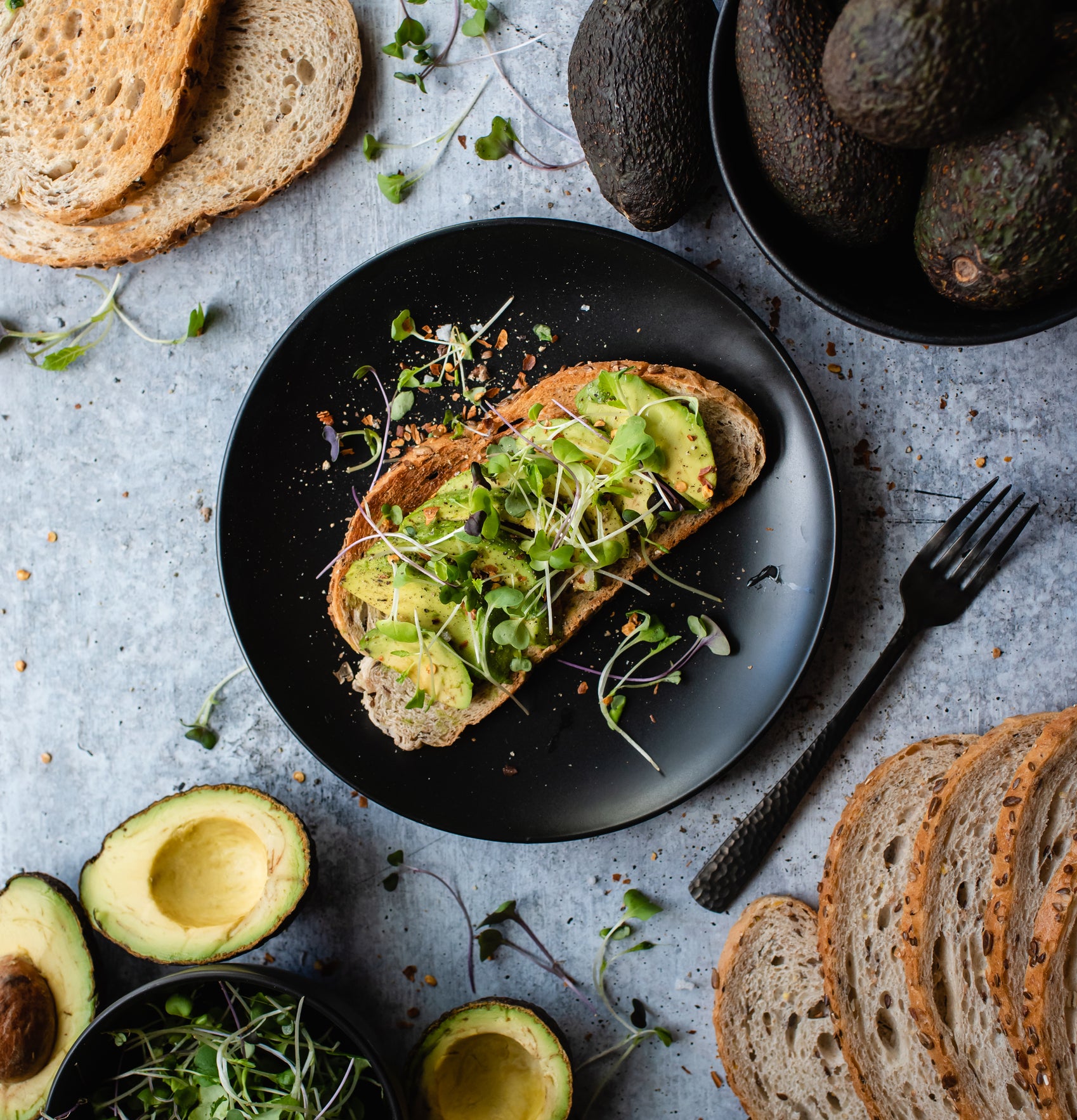 Avocado toast on a plate with ingredients around it on stone counter.