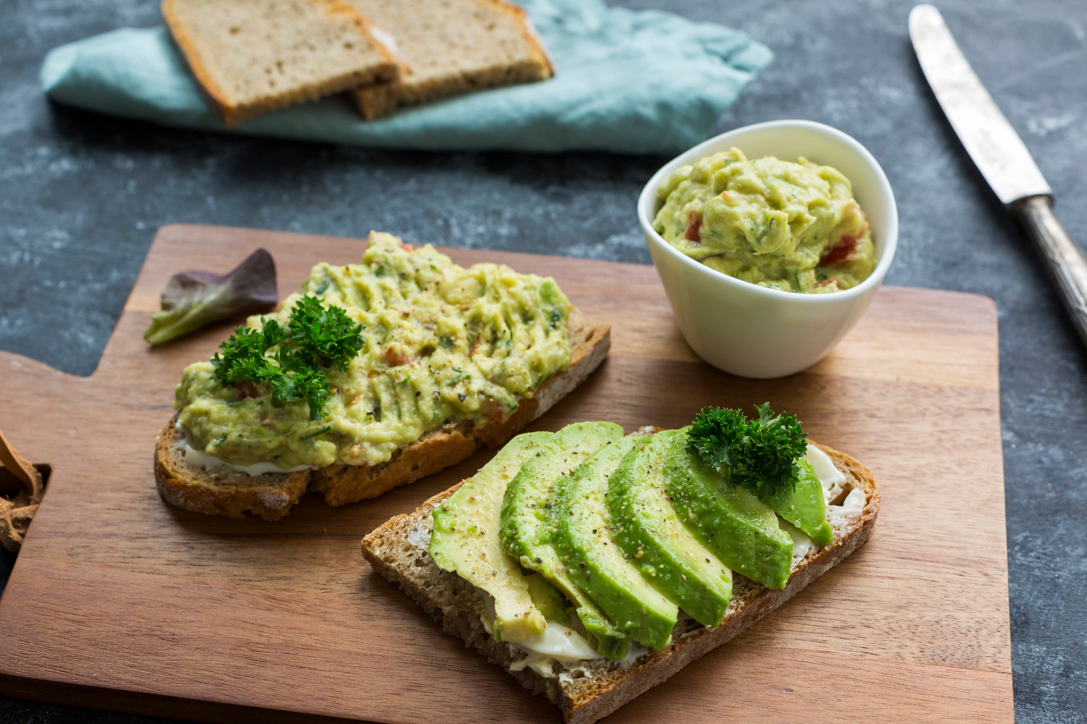 Slices of bread with sliced avocado and avocado cream on wooden board